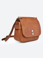 “Tan leather sling bag with gold hardware and front twist-lock closure against a light background.”