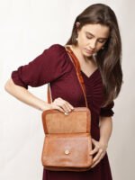 “Tan leather sling bag with gold hardware and front twist-lock closure against a light background.”