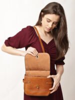 “Tan leather sling bag with gold hardware and front twist-lock closure against a light background.”